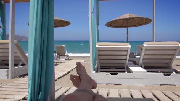 晴れた夏の日の間に海の近くのサンラウンジャーでリラックスして横断足を持つ男 — ストック動画