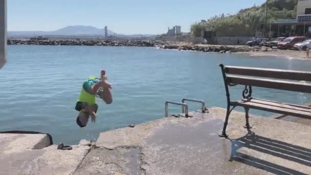 若いです男の子バックフリップしながら 日当たりの良い海の水に飛び込む — ストック動画