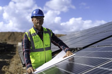 Güvenlik kaskındaki erkek mühendisin portresi güneş istasyonundaki bir güneş paneli sisteminin planlarını kontrol ediyor.