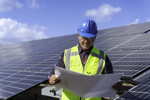 Portrait of male manager engineer in safety helmet checking with blueprint an operation of solar panel system at solar station