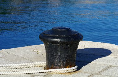 A black metal pole for mooring ships wrapped in a white thick rope in a seaport
