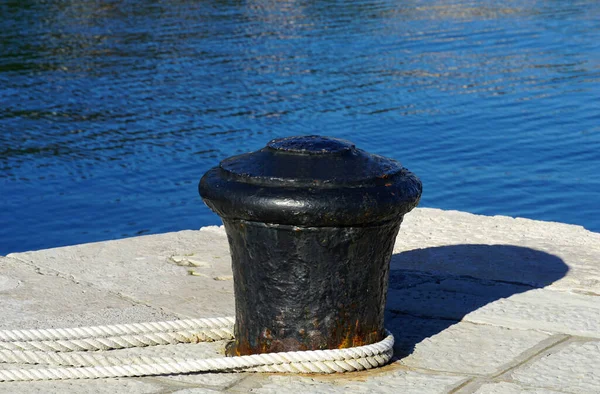 A black metal pole for mooring ships wrapped in a white thick rope in a seaport