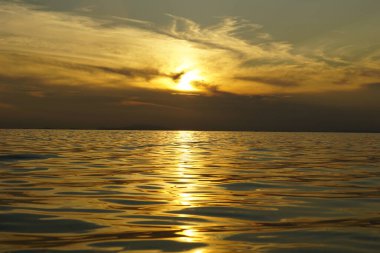 Deniz dalgalarının altın parıltısı dramatik gökyüzünün altında yaz günbatımında