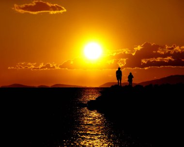 Yoğun turuncu gün batımı. Parlak aydınlanmış arka planda siyah bir siluet var.
