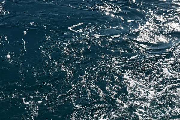 Swirling sea water with bright spots of sun glare on the surface