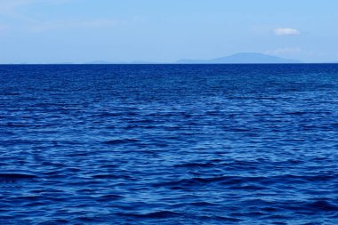 Kederli gökyüzü ve dalgalı deniz yüzeyi ile açık deniz ufku koyu mavi tonda