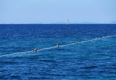 Denizin mavi dalgalı yüzeyi ve ufukta gezinen yatın havadan görünüşü.