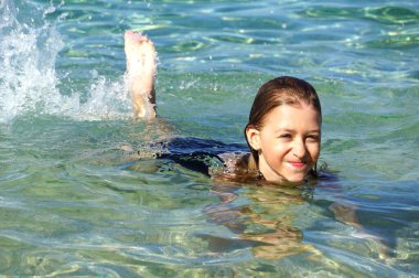 10 yaşında gülümseyen bir kız kumlu sahilde yüzmekten zevk alır.