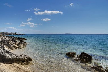 Mavi gökyüzü yumuşak kümülüs bulutlarıyla parlak turkuaz ve şeffaf deniz suyu üzerinde