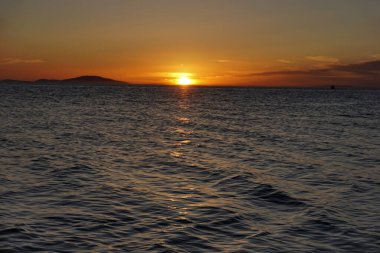 Pürüzsüz bir gün batımı üzerinde güzel mor dalgalı deniz yüzeyi üzerinde güneş parlıyor.