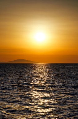 Dalgalı deniz yüzeyinin üzerinde güzel, ılık bir gün batımı.