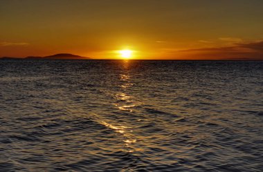 Sakin yaz günbatımında deniz kıyısında ipeksi ve pürüzsüz bir deniz yüzeyi.