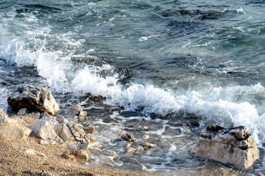 Büyük beyaz su sıçrayan temiz deniz suyu ve çakıl taşlı sahile vuran köpüklü dalga.