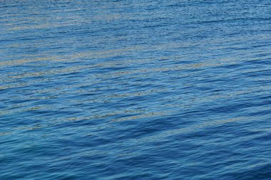 Mavi deniz suyunun tepesinde küçük dalgalarla altın ışık yansıması