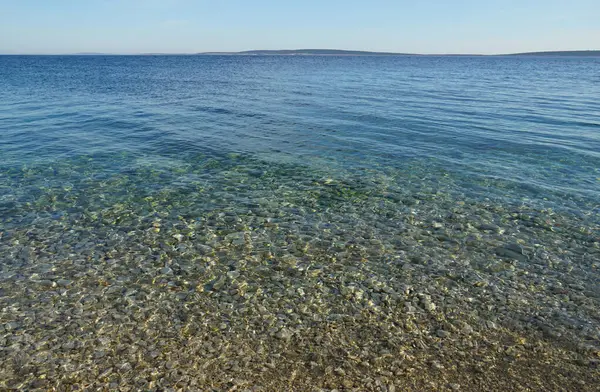 Turkuaz denizin üzerindeki deniz ufkuna havadan bakan el değmemiş doğadaki çakıl taşı plajı.