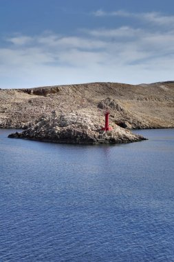 Kayalık bir sahil kenarında kırmızı feneri olan küçük kayalık bir adanın havadan görünüşü.