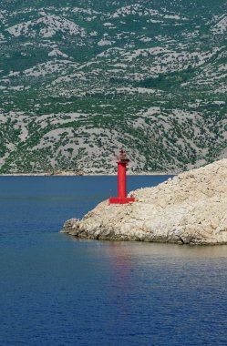Devasa bir dağın önündeki küçük kırmızı deniz feneri, taşımacılık ve yolcu gemileri için bir deniz geçidini gösterir.