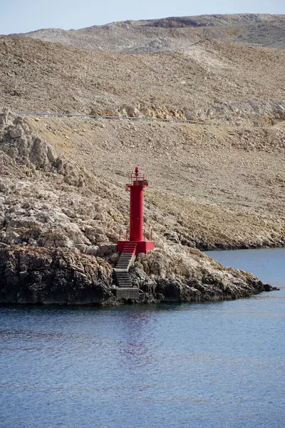 Gök mavisi denizdeki kayalık bir adada küçük bir deniz fenerinin dikey fotoğrafı.