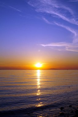 Parlak deniz yüzeyinin üzerinde canlı gün batımı canlı morumsu, sarı ve turuncu renkler