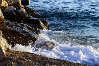 Taşlı kıyıya vuran su sıçrama dalgaları köpüren beyaz deniz köpüğü oluşturur.