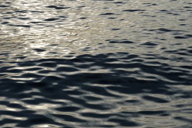 Deniz suyunun dalgalı yüzeyinde parlak bir yansımayı temsil eden metalik bir soyut.