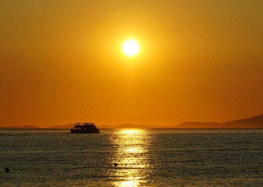 Yaz mevsiminde deniz kıyısında altın saatinde bir turist teknesinin silueti.
