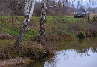 Sisin içinde sonbahar gölünün kıyısında bir cip.