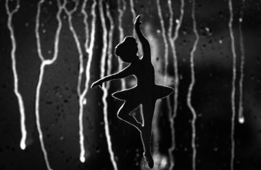 Küçümseyen damlalarla arka planda dans eden bir balerin silueti.