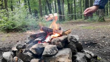 Bir adam ormandaki bir ateşte mashmerlow kızartıyor.