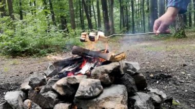 Bir adam ormandaki bir ateşte mashmerlow kızartıyor.