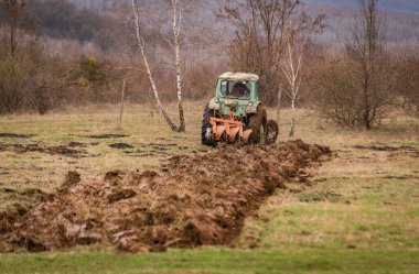 Eski bir traktör kırsal bir dağlık alanda toprağı sürüyor.