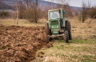 Eski bir traktör kırsal bir dağlık alanda toprağı sürüyor.