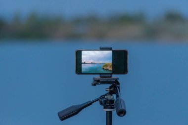 Bir dağ gölü manzarasını akıllı bir telefonla filme çekmek.