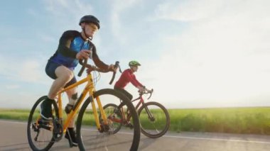 Spor giyimli, kasklı ve güneş gözlüklü profesyonel yarış motorcuları asfalt yolda güzel yeşil doğayla geziyorlar. Spor ve eğitim anlayışı.