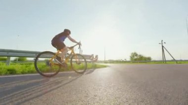 Beyaz erkek sporcu gün batımında bisiklet üzerinde sıkı çalışıyor. Genç bisikletçi her gün asfalt yolda egzersiz yapıyor..