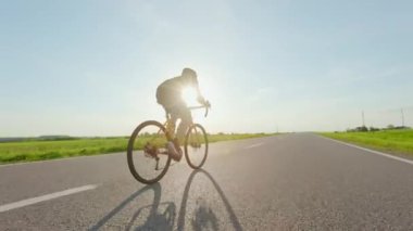 Sert dayanıklılık eğitimi sırasında asfalt otoyol boyunca bisiklet süren erkek bisikletçinin arka görüntüsü. Spor ve sağlıklı aktivite kavramı.