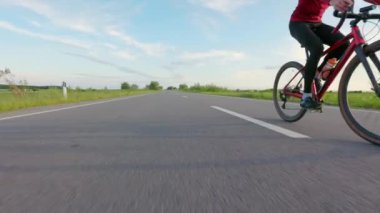 Mavi gökyüzü ve arka planda yeşil çimlerle triatlon yarışmasına hazırlanan sporcular. İki beyaz erkek karbon bisikletle ülke yolunda yarışıyor..