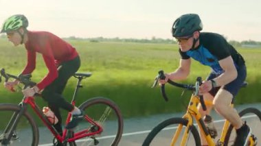 Arka planda yeşil çimlerle otoyol boyunca yüksek hızda bisiklet süren iki atlet grubu. Spor giyim rekorunu kırmaya çalışan erkekler pedal çeviriyor..
