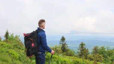Kulaklıklı, gezen, yürüyüş yapan, tepenin üstünde duran erkek turistin arka görüntüsü. Sırt çantası takan, dinlenen, doğanın güzelliğine hayran olan bir adam. Turizm ve yürüyüş kavramı.