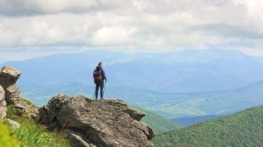 Genç bir erkeğin seyahat edişinin, yürüyüşünün, kayaların ve tepelerin üzerinde duruşunun arka görüntüsü. Turist sırt çantası takıyor, el kaldırıyor, dinleniyor, manzaranın tadını çıkarıyor. Turizm ve yürüyüş kavramı.