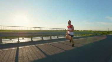 Enerjik koşucu eğitiminin ön görüntüsü, açık havada yoğun egzersiz. Sporcu, erkek sporcu sıcak yaz aylarında yolda koşuyor. Spor ve dayanıklılık kavramı.