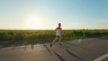 Genç sporcunun koşuşunu, kırsal kesimde yolda koşuşunu. Şort, tişört ve spor ayakkabı giyen erkek sporcu maratona katılıyor. Spor anlayışı ve sağlıklı yaşam tarzı.