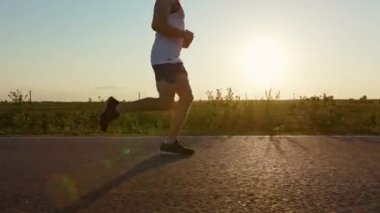 Maratona katılan genç, erkek sporcuları yakından takip edin. Kaslı bir sporcu, gün batımında dışarıda egzersiz yapıyor. Spor ve koşu kavramı.