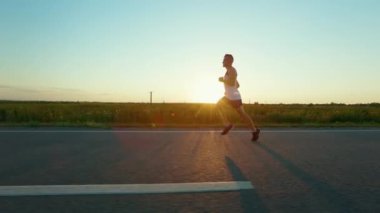 Yaz akşamları gün batımında koşan erkek sporcunun yan görüntüsü. Sporcu yarışmaya katılıyor, maraton koşuyor, egzersiz yapıyor. Spor ve koşu kavramı.