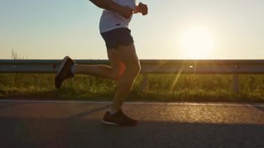 Gün batımında yolda koşan kaslı genç bir erkek. Sporcu, spor kıyafetleri ve spor ayakkabıları giyen sporcu, egzersiz yapan, dışarıda koşan. Spor ve spor anlayışı.