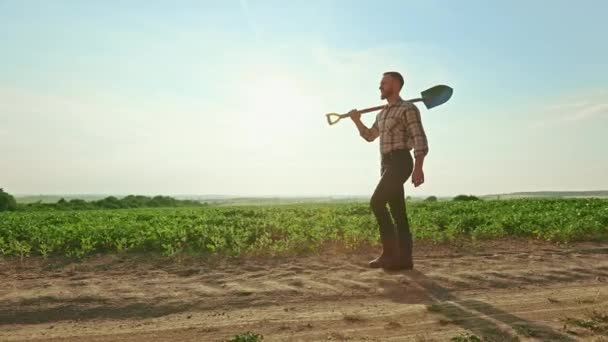 夏天阳光充足的情况下 男性农民在田里干活的侧视图 一个留着胡子 穿着格子呢衬衫 穿着橡胶靴的人在挖掘 种植植物和农业的概念 — 图库视频影像