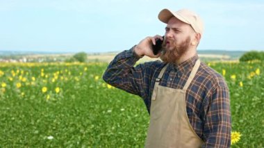 Tarlada çalışan, telefonla konuşan erkek çiftçinin yan görüntüsü. Sakallı bir adam tarlada ayçiçeği yetiştiriyor. Kırsalda çalışma kavramı.