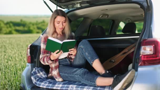 乗客の側のビューでは 観光客の車のトランクに座って ノートブックを保持 ブロンドの女性 カジュアルな服を着て旅行 旅と観光の概念 — ストック動画