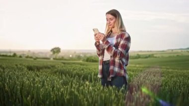 Çimlerin üzerinde akıllı telefon kullanan güzel bir kadının yan görüntüsü. Çekici, sarışın, mesajlaşan, konuşan, kaydıran, mesajlaşan, gülümseyen bir bayan. Modern yaşam tarzı kavramı.