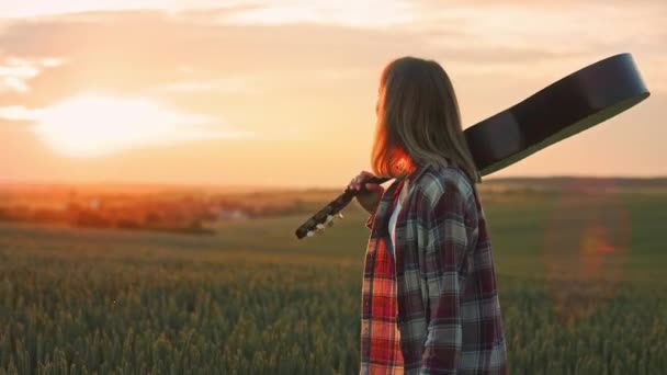 Gün Batımında Elinde Gitarla Sahada Yürüyen Sarışın Bir Kadın Neşeli — Stok video